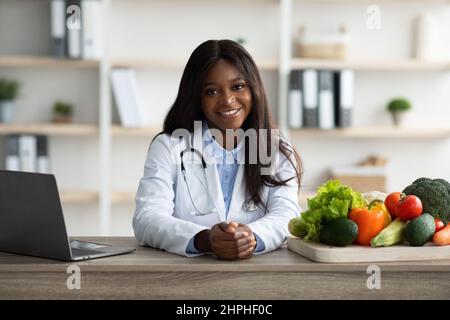 Concetto di alimentazione intelligente e sana. Ritratto di dietista femminile sorridente alla macchina fotografica, seduto sul posto di lavoro Foto Stock