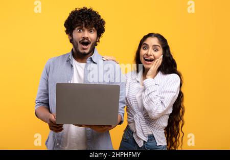 Offerta stupefacente, buon luogo. Sorpresi marito e moglie indiani che tengono un computer portatile e guardano la macchina fotografica a bocca aperta Foto Stock