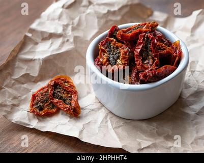 Metà pomodori secchi in un recipiente bianco sul tavolo di legno. Pomodori rossi disidratati con erbe e spezie. Cucina italiana Foto Stock