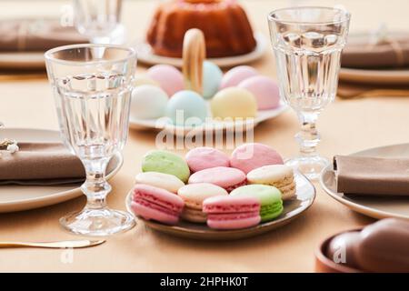 Primo piano di deliziosi piatti di macaroon su un elegante tavolo da pranzo decorato per Pasqua e primavera, spazio copia Foto Stock