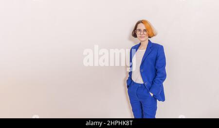 Elegante donna da lavoro in tuta blu per pantaloni, occhiali e capelli multicolore sui supporti per la testa Foto Stock