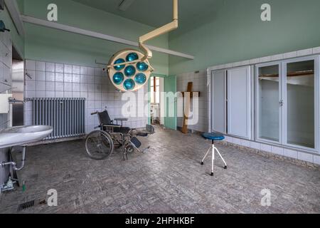 Sedia a rotelle in un ospedale abbandonato e creepy. Sullo sfondo un'antica croce grave nell'opera Foto Stock