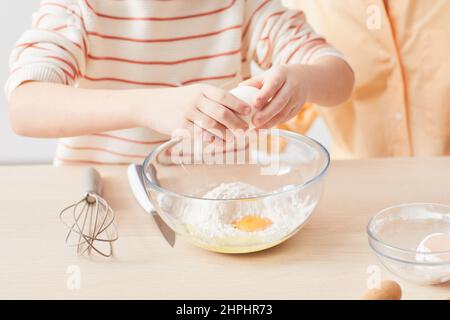 Primo piano di bambino rompere le uova mentre aiuta la madre a cuocere in cucina, spazio copia Foto Stock