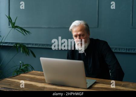 Medio scatto di un uomo maturo che guarda il training aziendale, webinar online sul lavoro in remoto su notebook o apprendimento a distanza da casa. Foto Stock