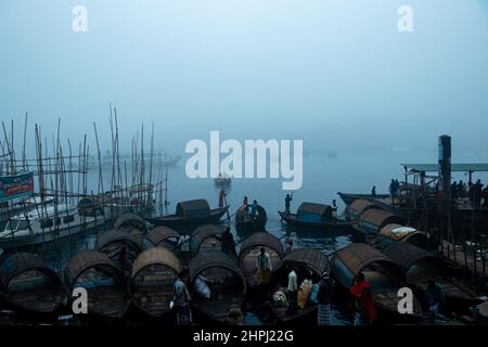 Narayanganj, Dhaka, Bangladesh. 22nd Feb 2022. I barcaioli sulla riva del fiume Shitalakhya aspettano che i passeggeri li infila attraverso il fiume in piccole barche di legno durante una mattinata d'inverno nebbia a Narayanganj, Bangladesh. Questo fiume è utilizzato come percorso verso l'area densamente popolata della città da milioni di lavoratori ogni giorno. Le navi di legno sono usate per trasportare la gente attraverso il fiume di Shitalakhya, che fluisce alla periferia della città di Narayanganj. (Credit Image: © Joy Saha/ZUMA Press Wire) Foto Stock