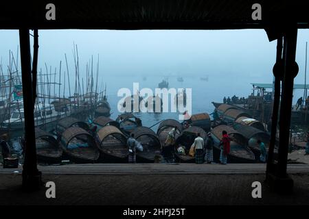 Narayanganj, Dhaka, Bangladesh. 22nd Feb 2022. I barcaioli sulla riva del fiume Shitalakhya aspettano che i passeggeri li infila attraverso il fiume in piccole barche di legno durante una mattinata d'inverno nebbia a Narayanganj, Bangladesh. Questo fiume è utilizzato come percorso verso l'area densamente popolata della città da milioni di lavoratori ogni giorno. Le navi di legno sono usate per trasportare la gente attraverso il fiume di Shitalakhya, che fluisce alla periferia della città di Narayanganj. (Credit Image: © Joy Saha/ZUMA Press Wire) Foto Stock