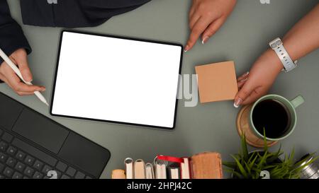 Due donne d'affari discutono di un piano sul tablet digitale e lavorano insieme nella moderna scrivania da ufficio. Mockup schermo vuoto tablet, note adesive, cancelleria a Foto Stock