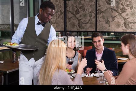 Cameriere afroamericano che serve pasti ad un'azienda amichevole Foto Stock