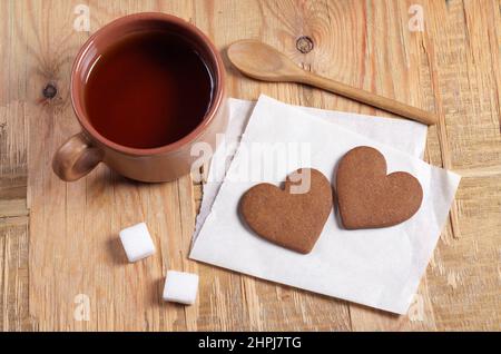 Biscotti di zenzero a forma di cuore e una tazza di tè situati sul vecchio sfondo di legno, vista ad angolo alto Foto Stock