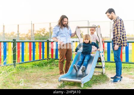 Ragazzino che gioca sul cursore del parco giochi con la sua famiglia Foto Stock