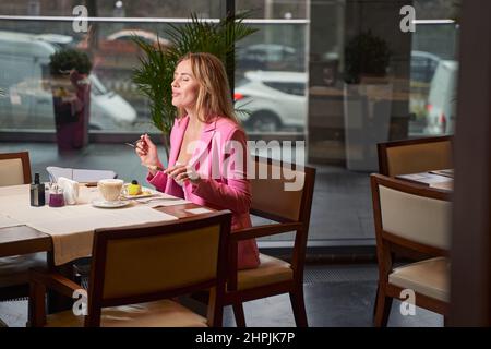 Felice signora bionda in cerca di soddisfazione con la sua scelta di dessert Foto Stock