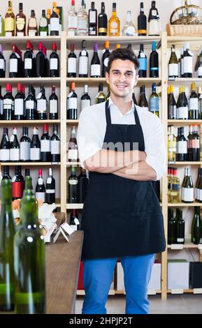 uomo venditore che indossa uniforme in piedi in negozio con vino Foto Stock