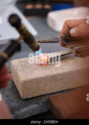 una donna che lavora nel suo laboratorio artigianale di gioielleria utilizzando una torcia su un anello per eseguire il suo lavoro su un blocco di pietra Foto Stock