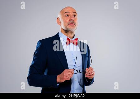 Scatto corto dell'uomo d'affari con il viso sorpreso che indossa il vestito e la cravatta di prua mentre si trova in piedi su sfondo grigio isolato. Spazio di copia. Foto Stock