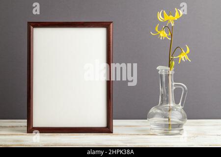 Cornice in legno con giglio di trota giallo o fiori viola a dente di cane in vetro su sfondo grigio pastello. Vista laterale, copia spazio, mockup, dima, primavera, su Foto Stock