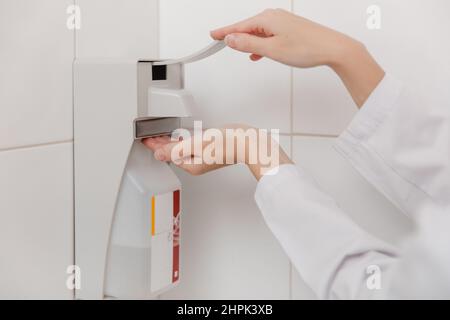 Il medico in uniforme bianca disinfetta le mani. Chirurgo lavaggio mani concetto ospedale. L'infermiere lava le mani con un igienizzatore o un dispenser o. Foto Stock