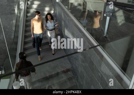 Due giovani dipendenti della moderna azienda high tech in abbigliamento formale si spostano al piano inferiore mentre discutono i punti del nuovo progetto tecnologico Foto Stock