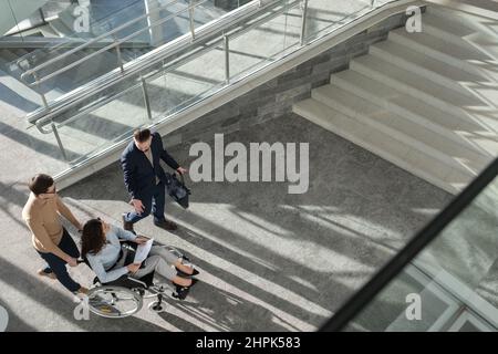 Al di sopra dell'angolo di CEO fiducioso spiegare la strategia aziendale a colleghi o partner disabili mentre si spostano in ufficio Foto Stock