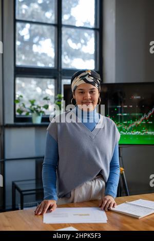 Giovane donna d'affari biraciale in piedi da tavolo contro schermo interattivo nella sala riunioni mentre insegna i colleghi al seminario Foto Stock