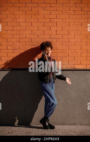 Giovane ragazza dai capelli scuri con un telefono su uno sfondo di muro di mattoni Foto Stock