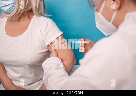Vaccinazione di una persona anziana. Il medico fa la vaccinazione alla donna anziana, portando la maschera facciale su sfondo blu. Foto Stock