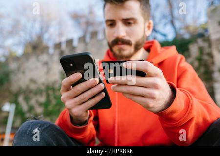 Acquisti online, uomo con carta di credito e smartphone. Comprare qualcosa in linea all'esterno. Bel uomo con una carta di credito e telefono cellulare fare Foto Stock