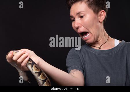 Foto di donna spaventata con pitone su sfondo nero Foto Stock