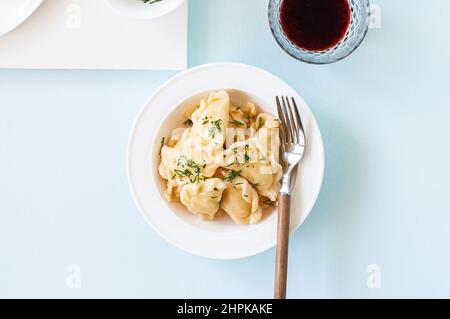 Deliziosi pierogi ripieni di patate con burro e verdure in un piatto bianco. Foto Stock