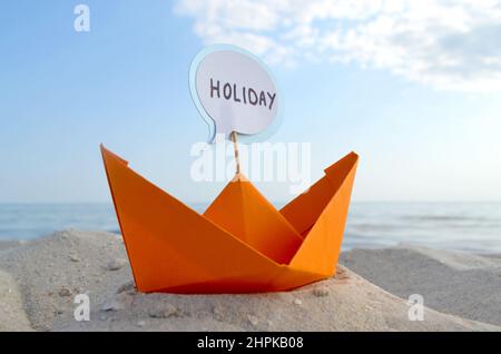 Orange Paper Boat su Sandy Seashore primo piano piccola barca da carta su sfondo Foto Stock