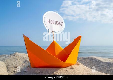 Orange Paper Boat su Sandy Seashore primo piano piccola barca da carta su sfondo Foto Stock