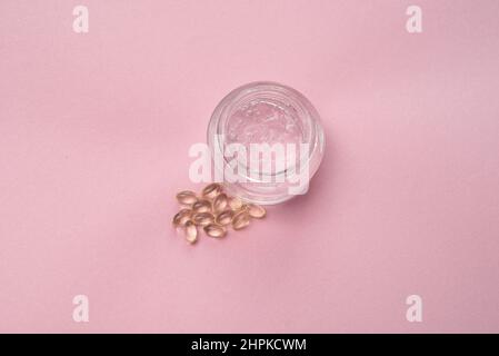 Gel con acido ialuronico in vaso di vetro e capsule su sfondo rosa Foto Stock