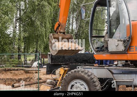 Escavatore con pala a benna con lavori di scavo in movimento terra o sabbia su un cantiere in un'area industriale. Foto Stock