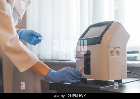 L'operatore di laboratorio inserisce il tubo del sangue nell'analizzatore di elettroliti animali. Foto Stock