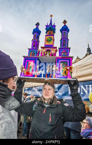 Uomo che porta la scena natività di Szopka in testa per la mostra durante il concorso annuale di dicembre, evento incluso nella lista del Patrimonio Culturale dell'UNESCO, al monumento Adam Mickiewicz, Piazza del mercato principale, Kraków, Polonia Foto Stock