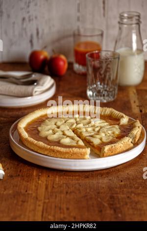 Torta di marmellata servita in ceramica bianca piatto in tavola di legno, verticale, piatti tazza e bottiglia di latte e succo in campo, bianco shabby sfondo Foto Stock