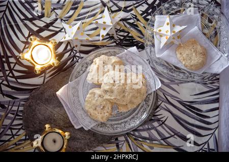 Biscotti al meringa e al choco di Natale serviti in un piatto di vetro e in un vassoio di pietra in un tavolo festivo con decorazioni e tealights Foto Stock