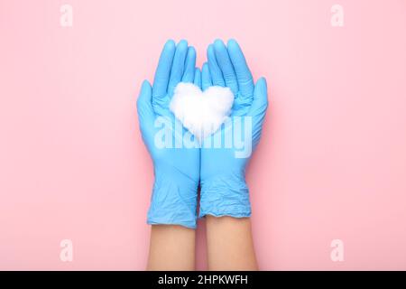 Mani femminili in guanti di gomma e cuore di lana di cotone su sfondo rosa, primo piano Foto Stock