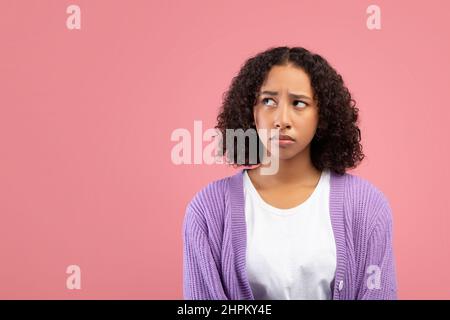 Giovane donna nera pensierosa che guarda da parte lo spazio vuoto sullo sfondo rosa dello studio Foto Stock