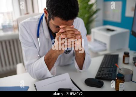 Depresso giovane medico di sesso maschile con mal di testa seduto nel suo ufficio Foto Stock