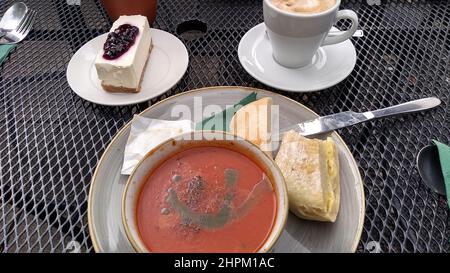 BEETHAM. CUMBRIA. INGHILTERRA. 08-22-21. Un tavolo all'aperto in una caffetteria con una ciotola di zuppa di pomodoro, una porzione di cheesecake e una tazza di caffè. Foto Stock