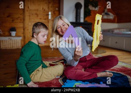 Un ragazzo con sindrome di Down seduto a terra e giocando con la nonna a casa Foto Stock