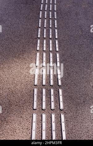 Primo piano di occhi di gatto metallici o marcatore di guida per pavimentazioni per catarifrangenti disabilitati modello di texture su asfalto. Foto di alta qualità Foto Stock
