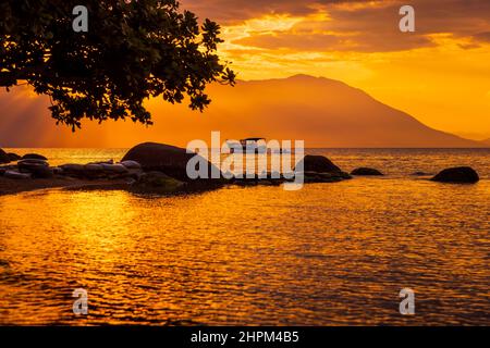 Caldo tramonto sulla spiaggia e mare tranquillo con barca a Florianopolis, Brasile Foto Stock