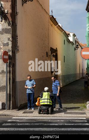 L'uomo in una sedia a rotelle motorizzata parla con due pedoni all'apertura di un vicolo al largo di Plaza de Adelantado nel sito Patrimonio Mondiale dell'Umanità di San C. Foto Stock