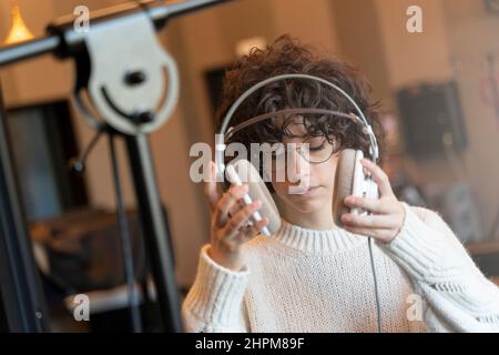 Una giovane cantante di capelli ricci con occhiali che registrano una canzone in un vero studio Foto Stock