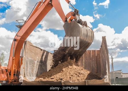 Lavori di scavo. La benna del trattore carica il terreno con una pala pesante nella parte posteriore di un autocarro di scarico sul cantiere. Foto Stock