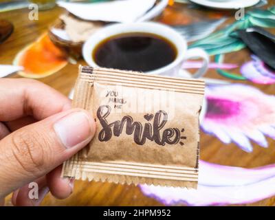 Busta di zucchero dove dice sorriso con una tazza di caffè sullo sfondo Foto Stock