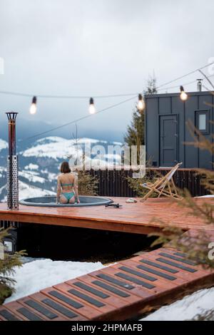 La donna nuota nel bagno caldo mentre riposa in una piccola casa moderna in montagna Foto Stock