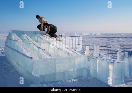 18 febbraio 2022 Russia, Listvyanka. Realizzare sculture di ghiaccio. Gli uomini livellano la superficie del blocco di ghiaccio. Foto Stock