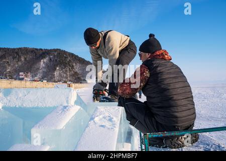 18 febbraio 2022 Russia, Listvyanka. Realizzare sculture di ghiaccio. Gli uomini livellano la superficie di un blocco di ghiaccio Foto Stock